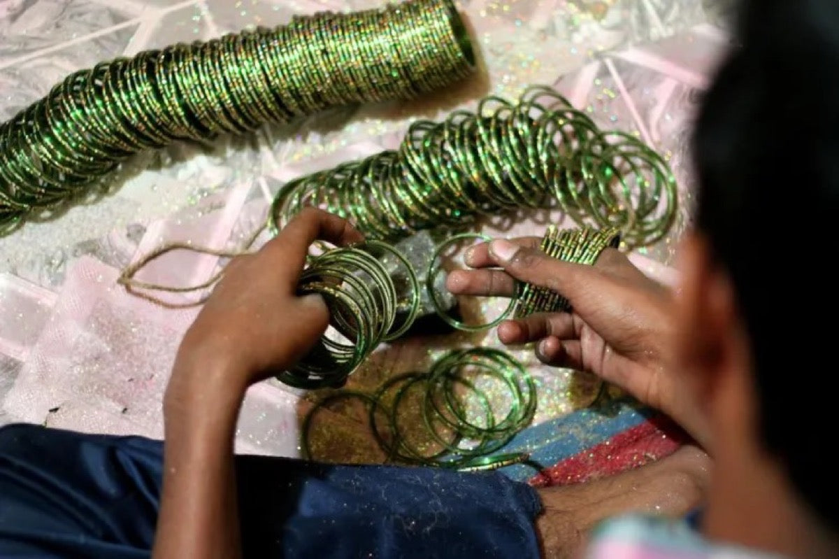 An artisan joining green glass bangles by hand